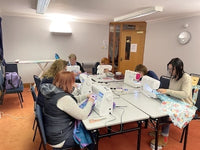 Group of people using sewing machines in a classroom setting.