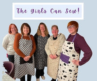 Group of women wearing aprons with 'The Girls Can Sew!' text above them.