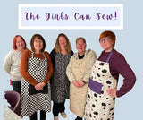 Group of women wearing aprons with 'The Girls Can Sew!' text above them.