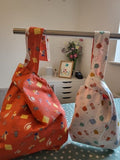 Two colorful bags hanging on a rack with a white dresser and decor items in the background.