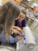 Two women working on a sewing machine in a workshop setting.