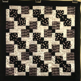A black and white quilt featuring a repeating geometric pattern of squares with polka dots, XOXO text, and solid colours, bordered by a solid black frame—a perfect inspiration for any patchwork and quilting course.