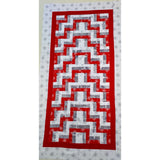 A rectangular quilted table runner with a zigzag pattern, ideal for a quilting for beginners course. Alternating red and white strips are bordered by red, with an outer border of grey snowflakes on a white background.