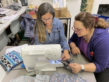 Two women working on a sewing machine in a workshop setting.