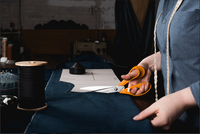 A woman cutting dressmaking fabric with a pair of Fiskars 25cm scissors