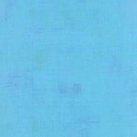A textured blue quilting fabric in the Moda Grunge range, with subtle variations in shade and faint, uneven patterns throughout.